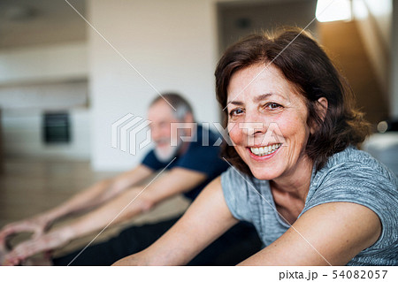 A senior couple indoors at home, doing exercise on the floor. 54082057
