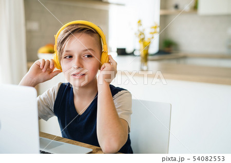 Small boy with headphones and laptop sitting at the table indoors at home. Small boy with headphones and laptop sitting at the table indoors at home. 54082553