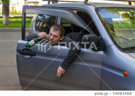 Drunk car driver with a bottle of beer in hand Drunk car driver with a bottle of beer in hand 54083468