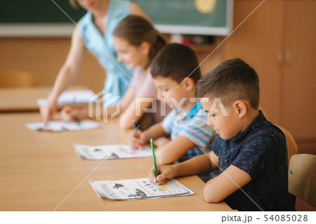 Teacher helping school kids writing test in classroom. education, elementary school, learning and Teacher helping school kids writing test in classroom. education, elementary school, learning and 54085028