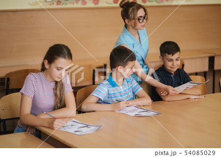 Teacher helping school kids writing test in classroom. education, elementary school, learning and Teacher helping school kids writing test in classroom. education, elementary school, learning and 54085029