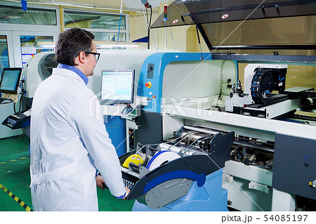 The engineer in a white robe and glasses works for the Surface Mount Technology machine. PCB The engineer in a white robe and glasses works for the Surface Mount Technology machine. PCB 54085197