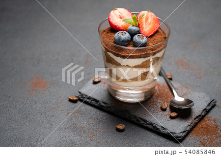Classic tiramisu dessert with blueberries and strawberries in a glass on stone serving board on dark 54085846