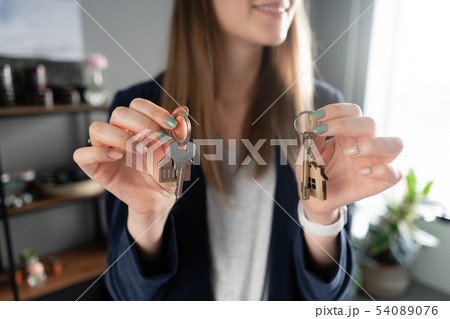 two house keys in womans hands. Young pretty woman smiles. Modern light lobby interior. Real estate 54089076