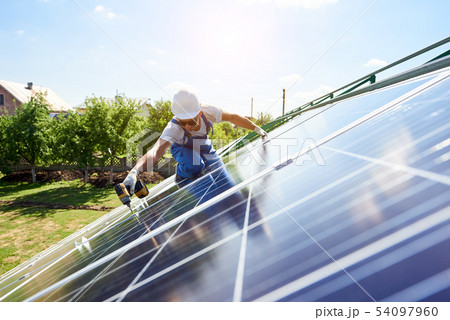 Worker mounting solar panels for renewable energy on house's roof. 54097960