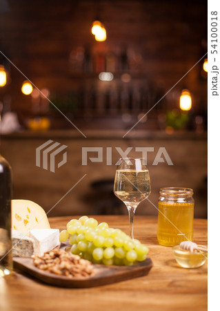 Cheese platter with fresh grapes and glasses of white wine on a rustic wooden table in a vintage pub Cheese platter with fresh grapes and glasses of white wine on a rustic wooden table in a vintage pub 54100018