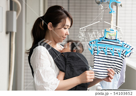 赤ちゃんを抱いて洗濯物を干す母親 育児 家事 54103652
