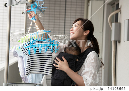 赤ちゃんを抱いて洗濯物を干す母親 育児 家事の写真素材