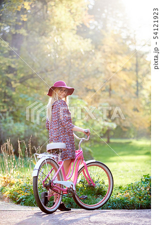 Blond fashionable long-haired attractive girl in short dress with lady bicycle in sunny park. Blond fashionable long-haired attractive girl in short dress with lady bicycle in sunny park. 54121923
