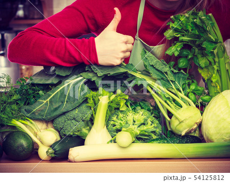 Woman in kitchen having many green vegetables 54125812