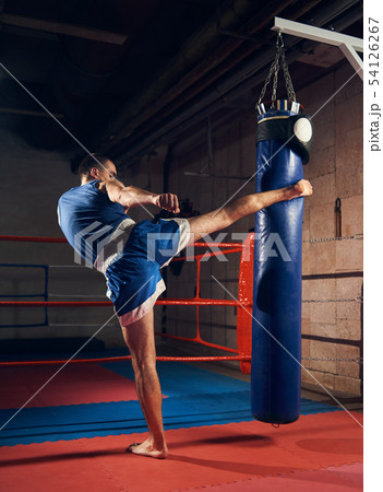 Handsome kick boxer training kicking and punching boxing bag 54126267