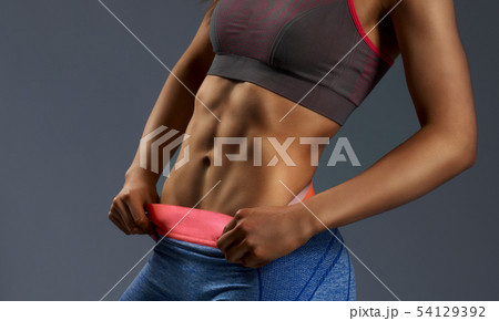 Close up of woman's abs with tanned skin on gray background Close up of woman's abs with tanned skin on gray background 54129392