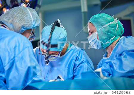 Surgeon performing cosmetic surgery in hospital operating room. Surgeon in mask wearing loupes Surgeon performing cosmetic surgery in hospital operating room. Surgeon in mask wearing loupes 54129568