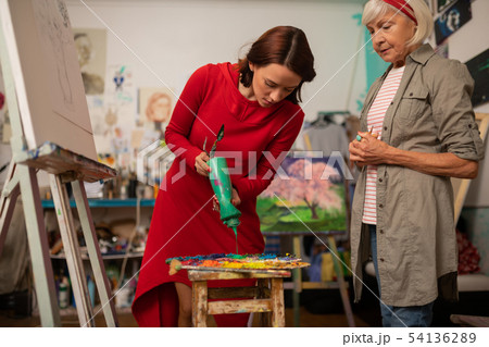 Dark-haired student pouring green gouache on color palette Dark-haired student pouring green gouache on color palette 54136289