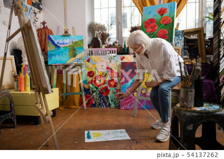 Artist putting paper on floor and sprinkling some paint Artist putting paper on floor and sprinkling some paint 54137262