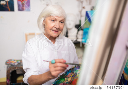 Appealing aged woman smiling while painting on canvas Appealing aged woman smiling while painting on canvas 54137304
