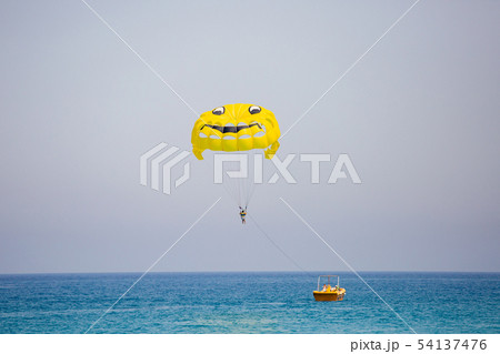 Woman flying on a yellow parachute with smiling face on it Woman flying on a yellow parachute with smiling face on it 54137476