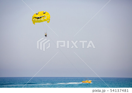 Couple of tourists flying on a yellow parachute with smiling face on it 54137481