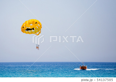 Three tourists flying on a yellow parachute with smiling face on it 54137505