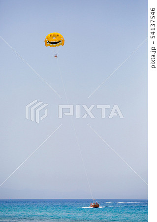 Three tourists flying on a yellow parachute with smiling face on it 54137546