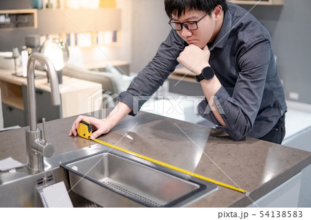 Asian man using tape measure on kitchen counter 54138583