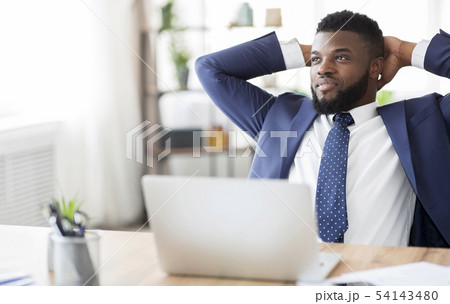 Satisfied african businessman sitting with behind head at workplace Satisfied african businessman sitting with behind head at workplace 54143480