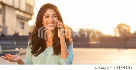 Happy woman talking on phone, walking in city Happy woman talking on phone, walking in city 54144155