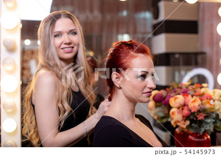 Beautiful, red-haired girl with long hair, hairdresser weaves a French braid, in a beauty salon 54145973