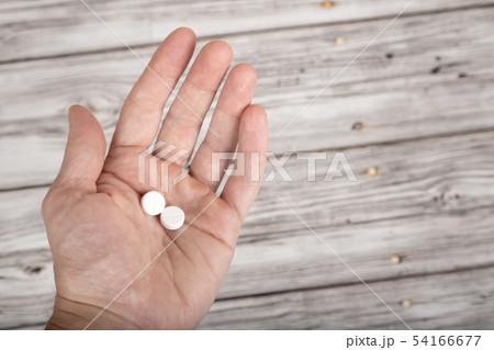 Male hand holding two tablets on wooden background 54166677