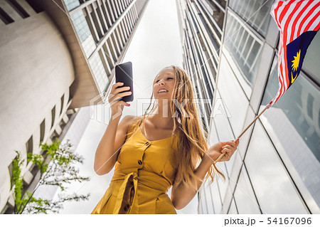 Travel and technology. Young woman tourist with the flag of Malaysia is looking at a city map in a 54167096
