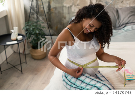 Expectant mother measuring her belly in bedroom. 54170743