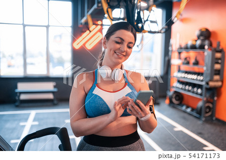 Young woman reading messages on phone before workout Young woman reading messages on phone before workout 54171173