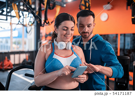 Dark-haired woman showing her old photos to her trainer Dark-haired woman showing her old photos to her trainer 54171187