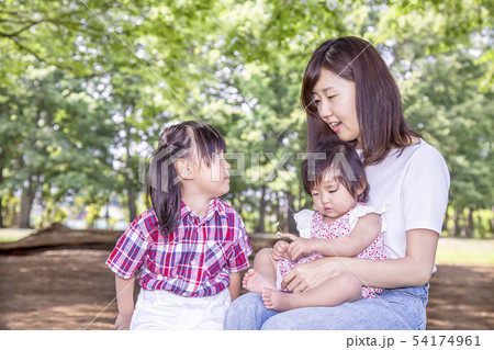 公園で緑の樹木をバックに遊ぶ母と幼い女の子3人。愛、幸せイメージ 54174961