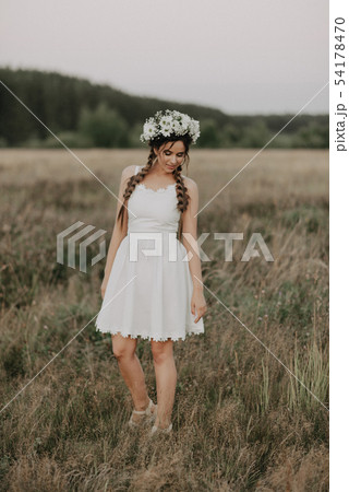 girl with braids and a floral wreath in a white boho dress in summer outdoors girl with braids and a floral wreath in a white boho dress in summer outdoors 54178470