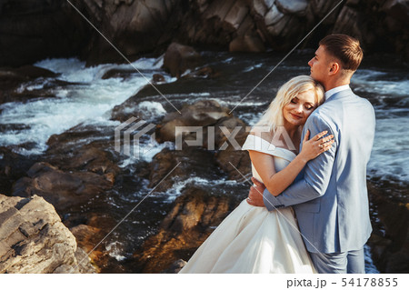 Amazing wedding couple, bride and groom holding hands on a mountains and rivers background. Cute Amazing wedding couple, bride and groom holding hands on a mountains and rivers background. Cute 54178855