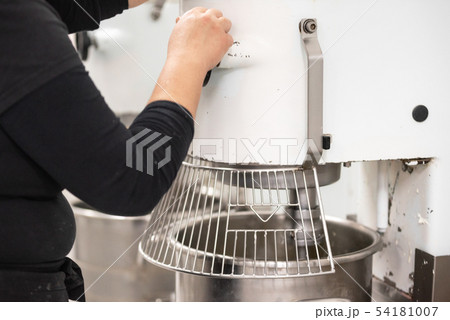 Confectionery factory worker standing and operating industrial dough mixer machine. Confectionery factory worker standing and operating industrial dough mixer machine. 54181007