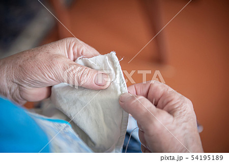 an elderly woman sews torn clothes. close-up of women's hands with thread and needle. the concept of 54195189