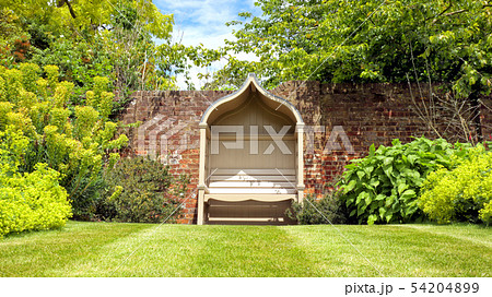 vintage wooden bench by brick wall in green garden 54204899