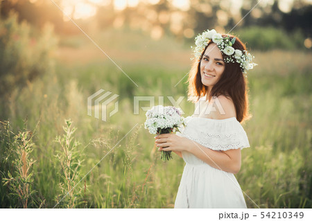 Caucasian happy girl in a white dress with a bouquet of flowers and a wreath in the summer 54210349