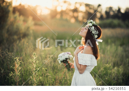 beautiful young girl with a bouquet of flowers and a wreath in a white dress 54210351