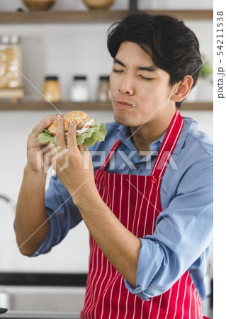 Asian man, he holds a hamburger and bites it. Asian man, he holds a hamburger and bites it. 54211538