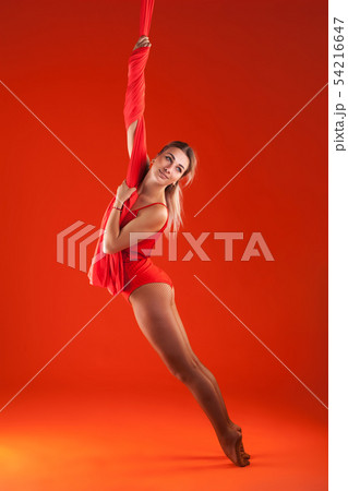 A young blonde girl with long hair in a red suit performs gymnastic and exercises on silk. 54216647