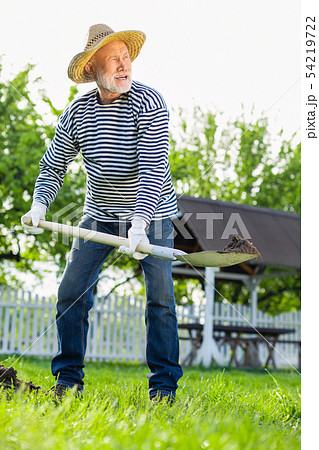Grey-haired man in straw hat using shovel while digging ground 54219722