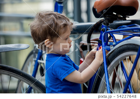 toddler boy plays enthusiastically with big bikes on a city bike parking 54227648