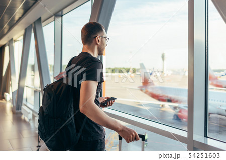 Man in airport near gate windows at planes on runway. 54251603