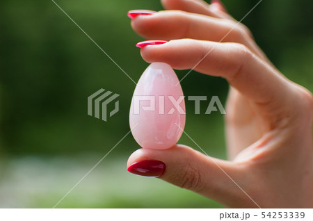 Close up photo of female hand holding a vaginal yoni egg. Rose quartz crystal egg on river 54253339