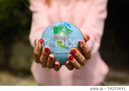 Young female teenager in pink casual clothes with red manicure holding a little globe in her hands Young female teenager in pink casual clothes with red manicure holding a little globe in her hands 54253641