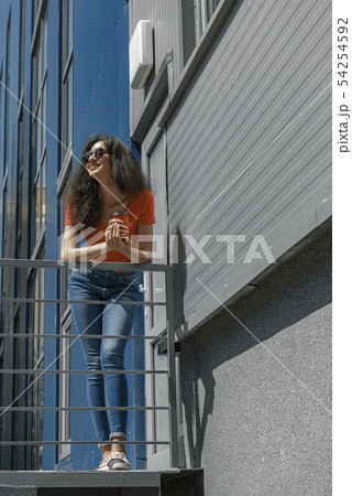 Beautiful young woman with coffee cup leaning on handrail Beautiful young woman with coffee cup leaning on handrail 54254592