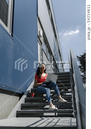 Charming young woman with laptop sitting on stairs Charming young woman with laptop sitting on stairs 54254611